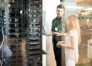 Two people with a laptop in front of server racks in a data center