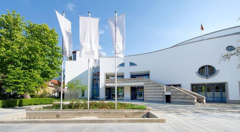 Weißes Verwaltungsgebäude des Landratsamts Schweinfurt mit Fahnen am Eingang
