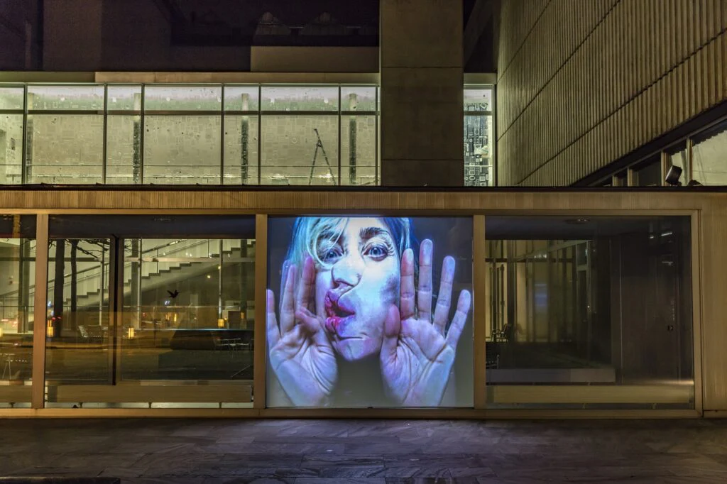Videoinstallation mit großem Gesicht in der Glasfassade des Kunsthaus Zürich bei Nacht