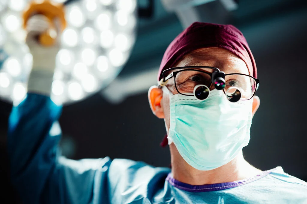 Person with magnifying glasses and face mask under surgical lights in the operating room