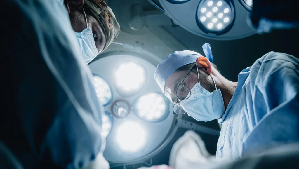 Two people in surgical attire under operating lights from the patient's perspective