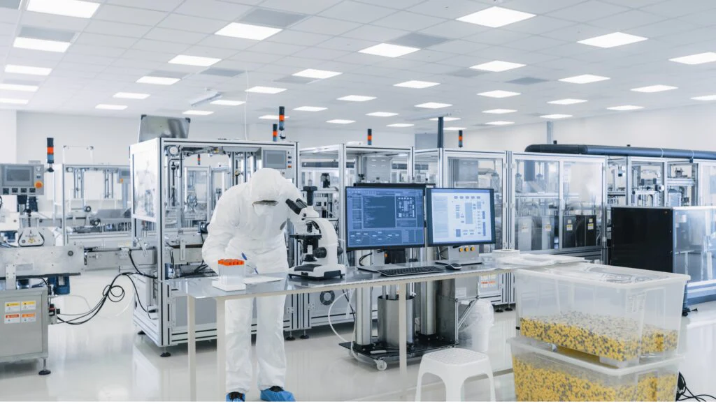 Person in protective suit at microscope in a production hall with laboratory equipment