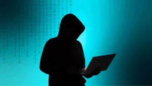Silhouette einer Person mit Laptop vor Binärcode als Sinnbild für Cyberangriffe
