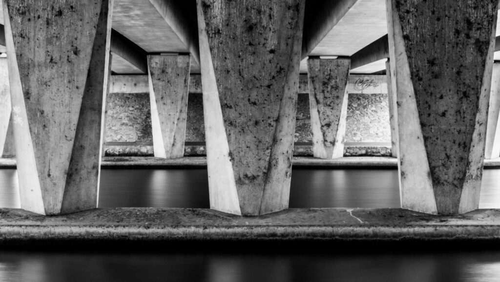 Betonpfeiler einer Brücke über Wasser in Schwarzweiß als Bild für ein tragfähiges Fundament